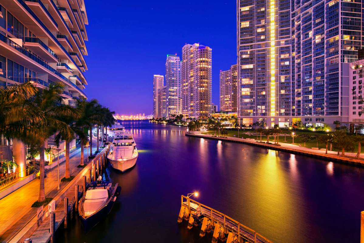 A waterfront view of illuminated skyscrapers and boats at night.