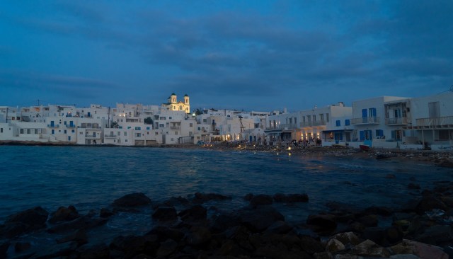 A coastal scene featuring white buildings along the shore under a twilight sky, with a church in the background.