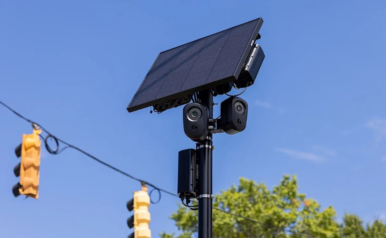A solar panel mounted on a pole with cameras and equipment, set against a clear blue sky.