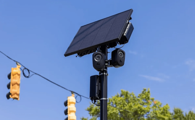 A solar panel mounted on a pole with cameras and equipment, set against a clear blue sky.