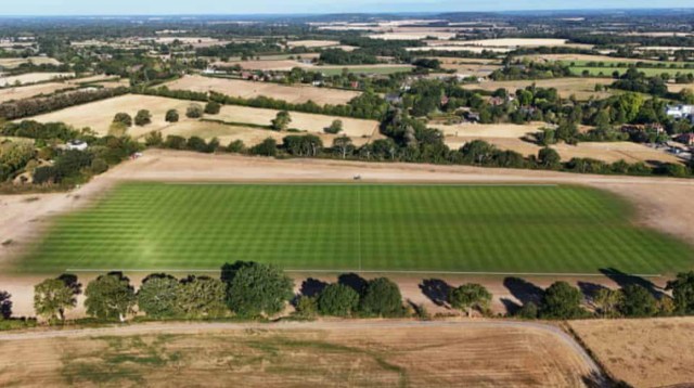 An aerial view of a dry landscape with a perfectly green polo field in the middle.