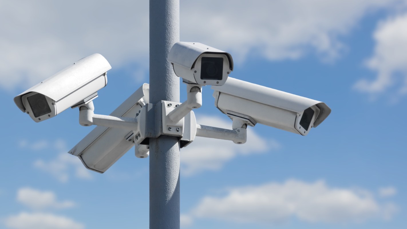 Multiple security cameras mounted on a pole against a blue sky.
