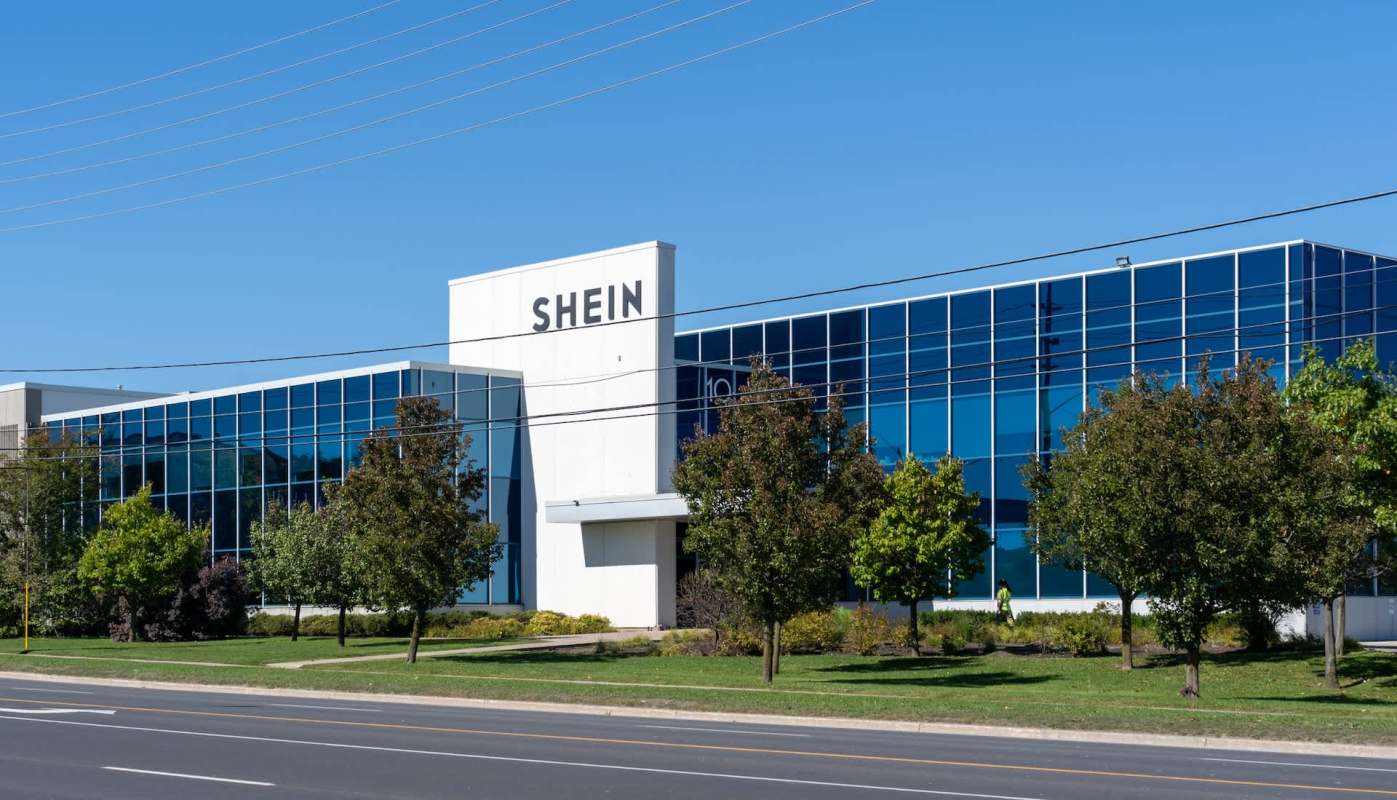 A modern building with large glass windows and a sign indicating "SHEIN," surrounded by green landscaping.