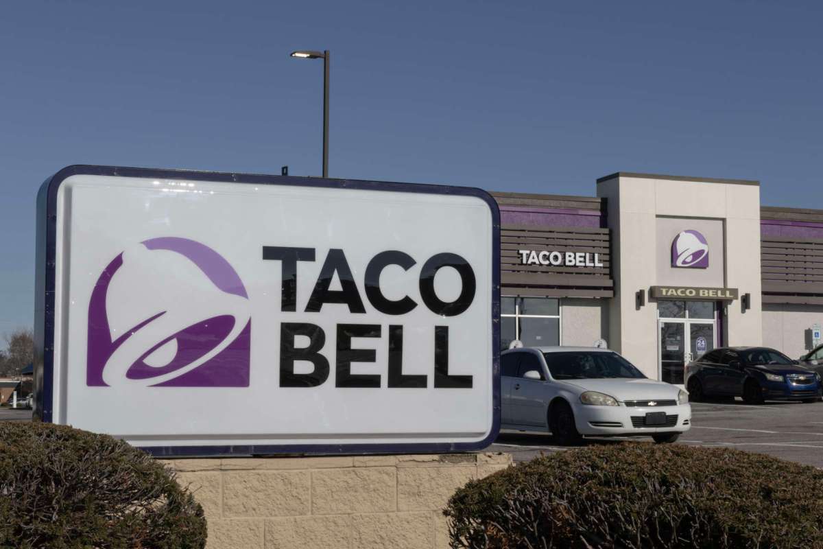 A Taco Bell restaurant with a large sign and parked cars in front.