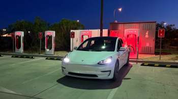 A Tesla vehicle parked at a charging station illuminated in red at night.