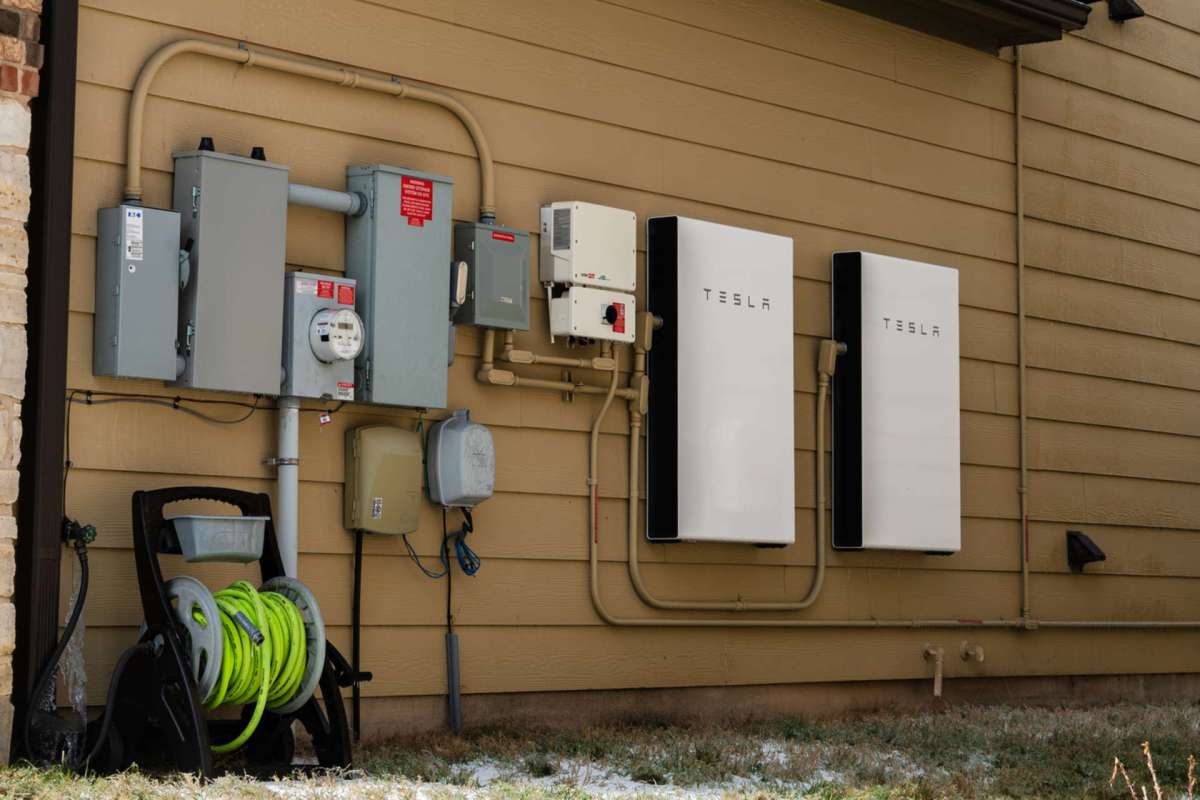 A wall-mounted electrical setup with two Tesla battery units and various electrical boxes.