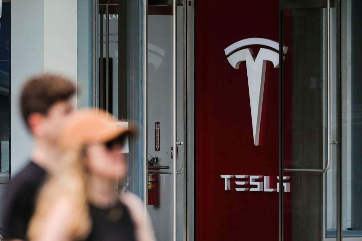 The entrance of a Tesla store, featuring the Tesla logo on a red wall.