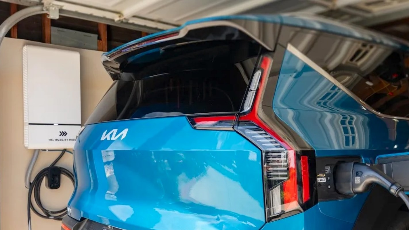 A blue electric vehicle charging in a garage next to a wall-mounted charging station.