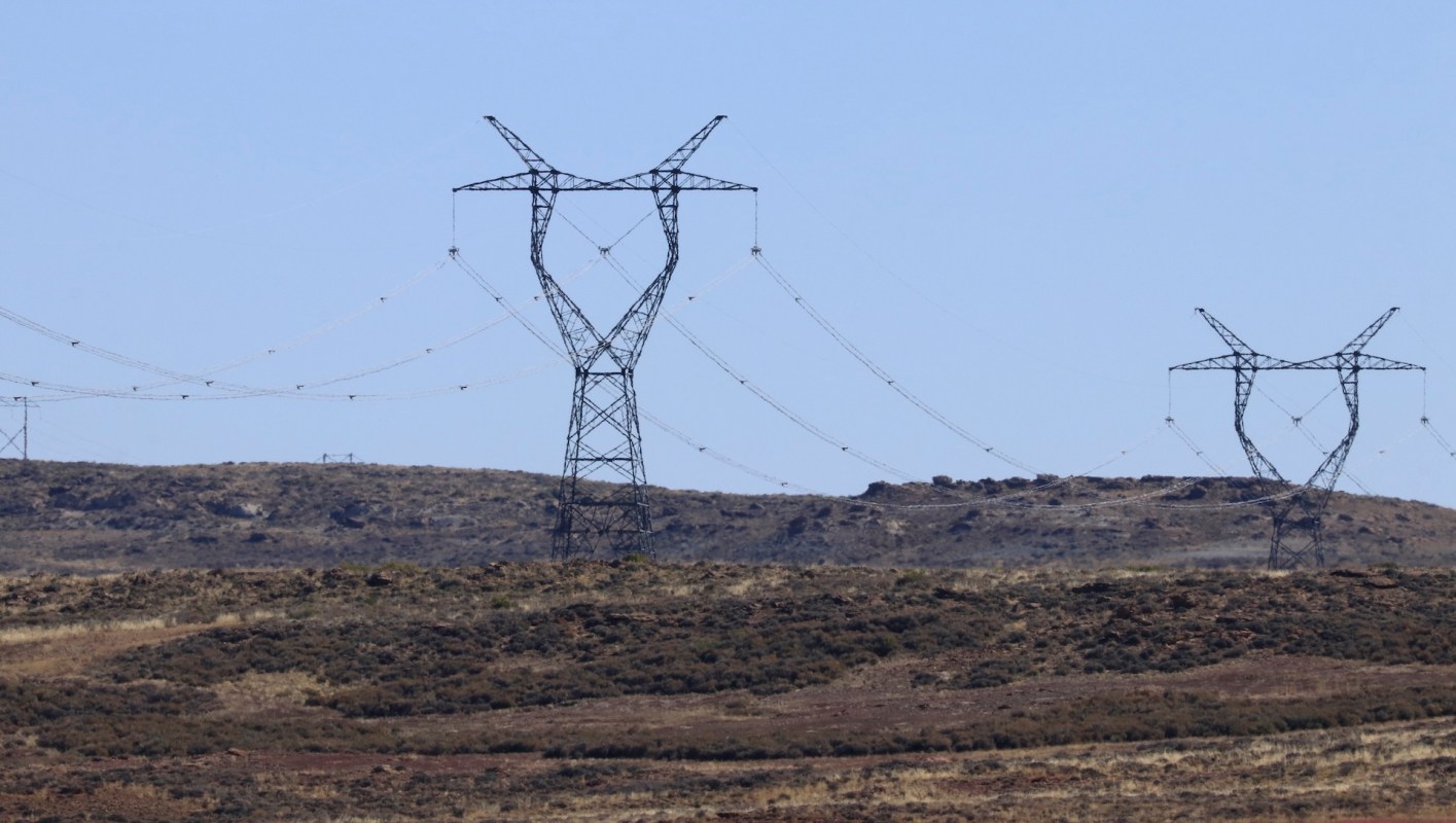 Power lines supported by tall pylons cross a dry landscape under a clear blue sky.