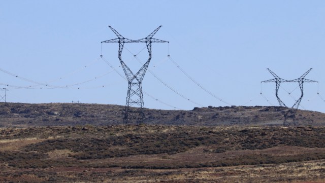 Power lines supported by tall pylons cross a dry landscape under a clear blue sky.