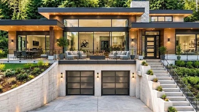 A modern house with large glass windows, a balcony, and landscaped steps leading to the entrance.
