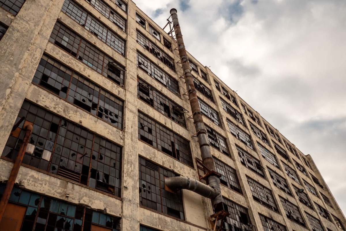 An abandoned industrial building with broken windows and a large exhaust pipe.