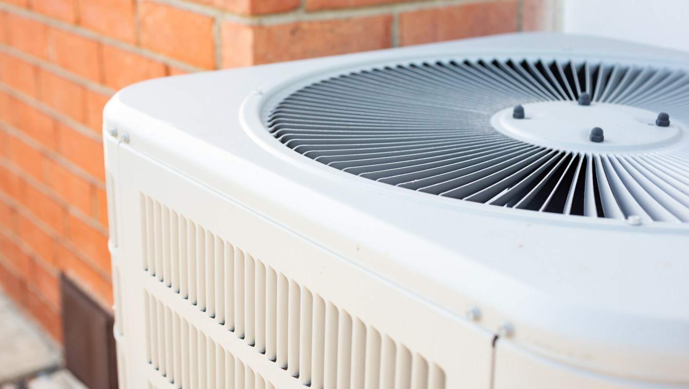 An air conditioning unit beside a brick wall.