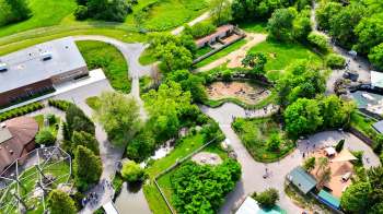 An aerial view of a landscaped park featuring pathways, greenery, animal enclosures, and visitors walking.