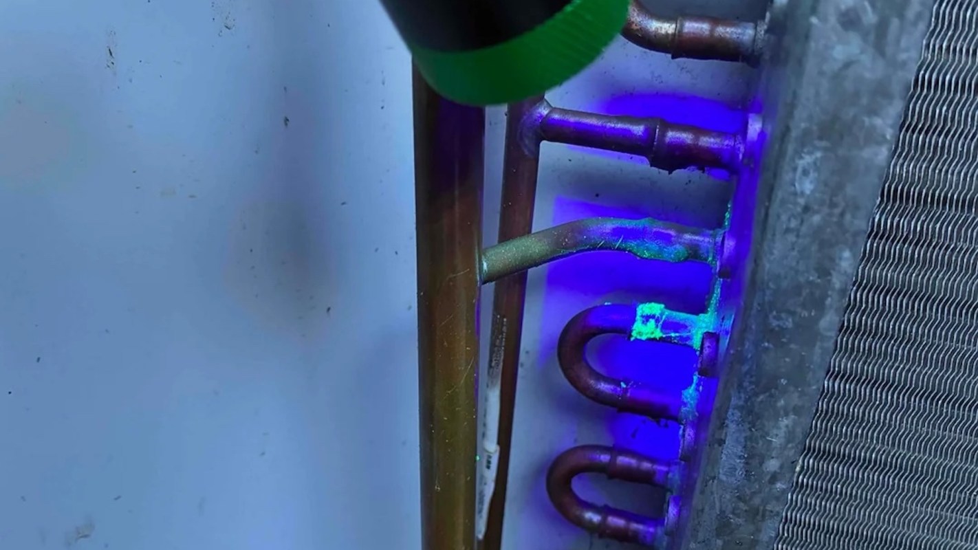 A close-up of metal pipes with a light source illuminating a green substance on the surface.