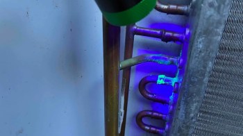 A close-up of metal pipes with a light source illuminating a green substance on the surface.