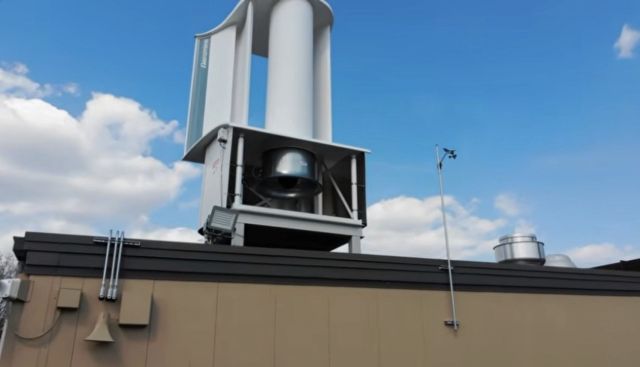 A wind turbine installed on a building roof with a clear sky in the background.