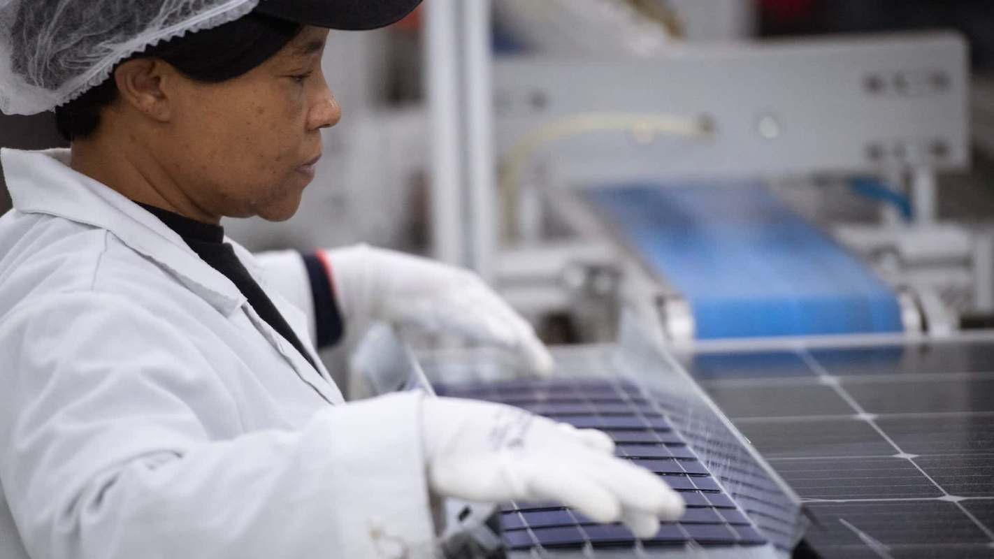 A woman works on assembling solar panels in a manufacturing facility.