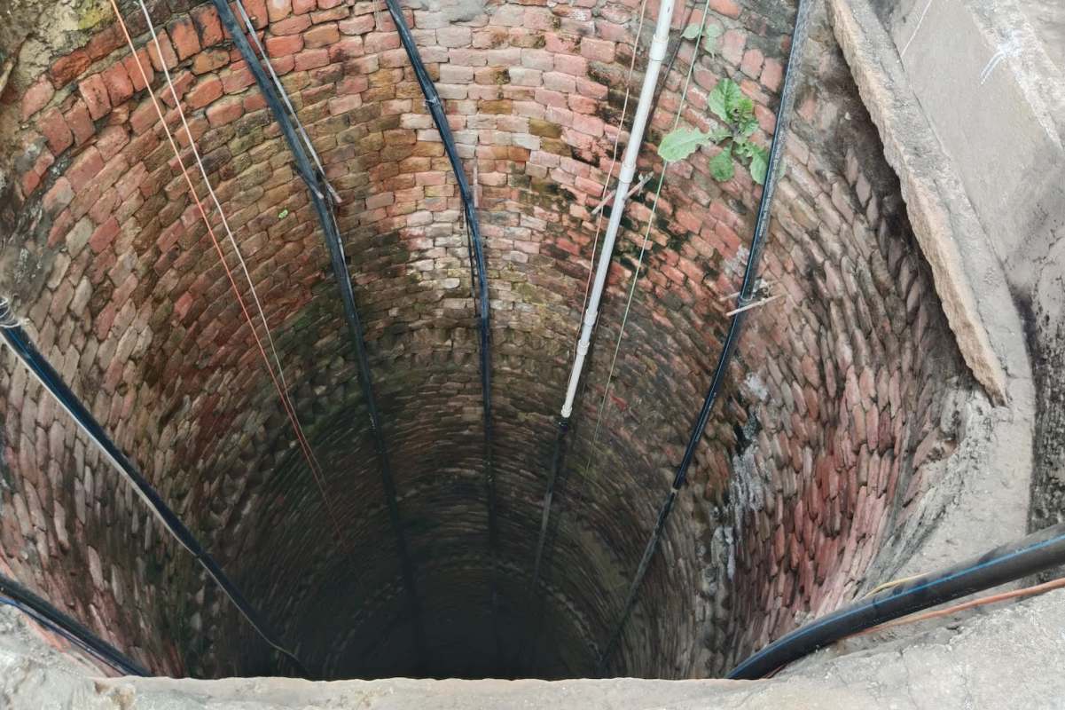 A view looking down into a deep brick well with visible pipes along the sides.