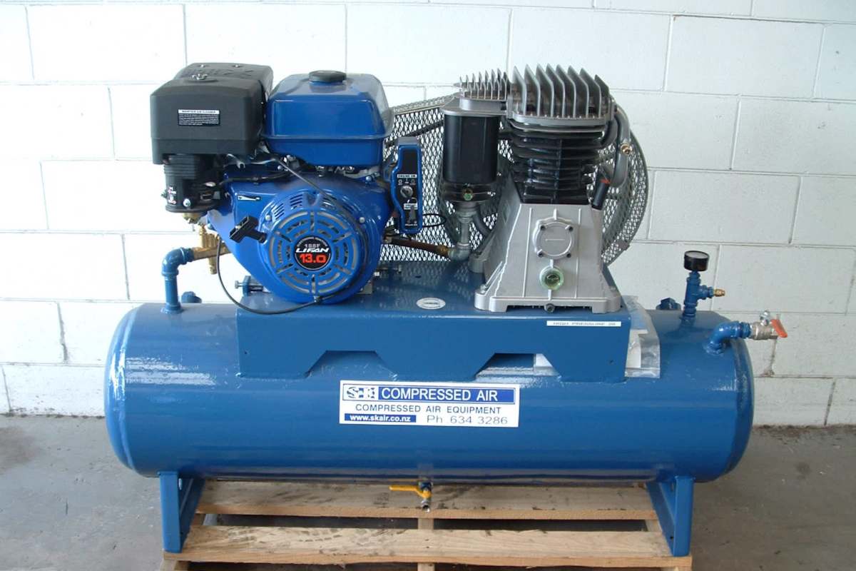 A blue air compressor with an attached motor and metal fittings on a wooden pallet.