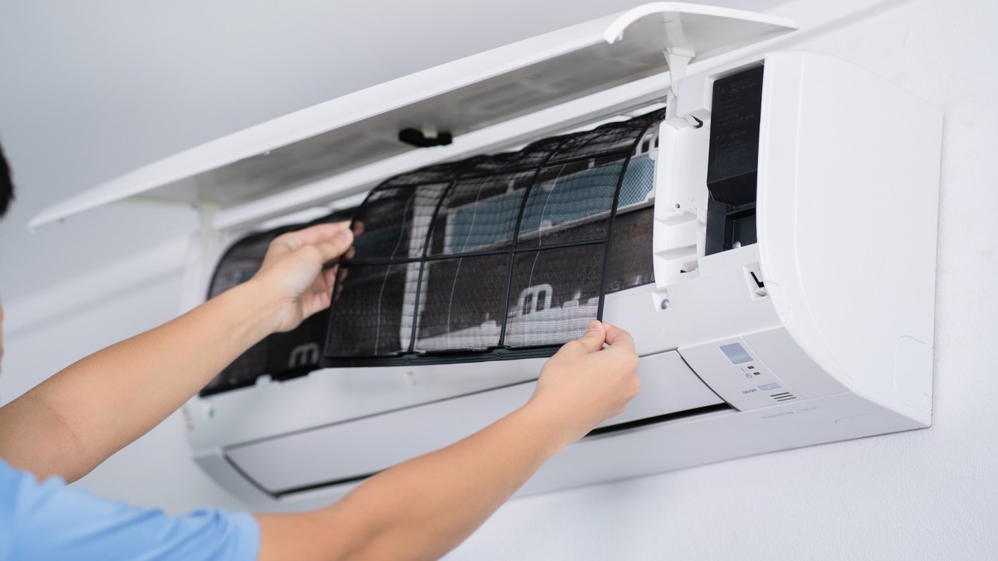 A person removes a filter from an air conditioning unit for cleaning.