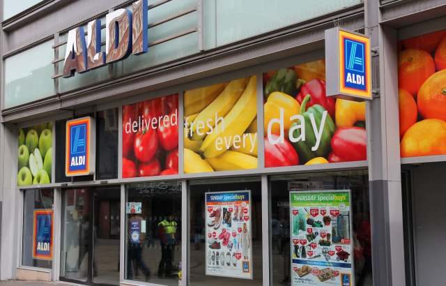 An Aldi store front featuring colorful fruit graphics and promotional posters.