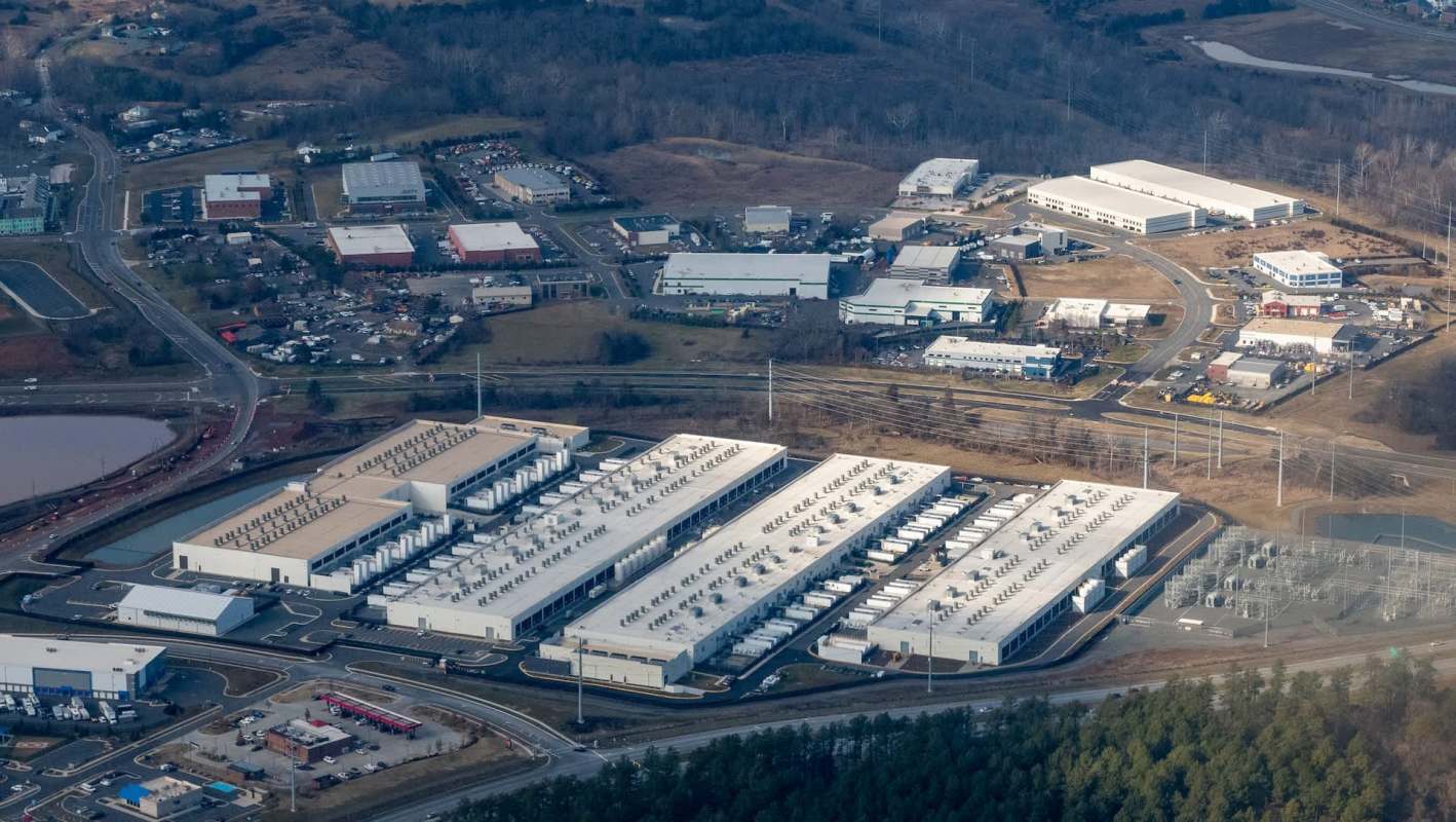 An industrial area with several large warehouses and roads, surrounded by fields and power lines.
