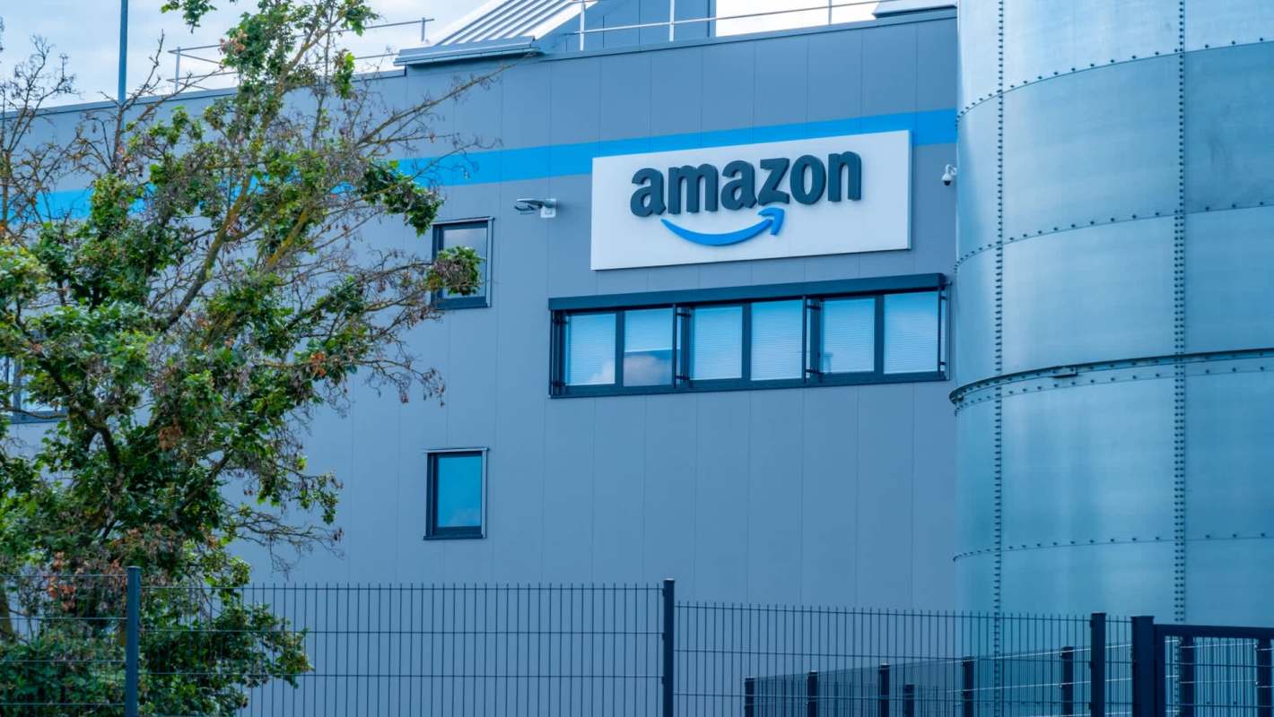 An Amazon facility with a visible logo and outdoor greenery in front.