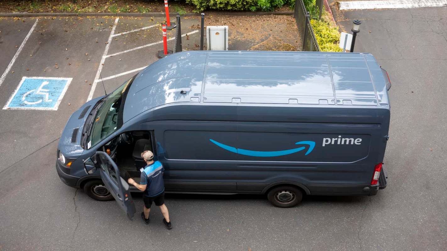 An Amazon Prime delivery van parked in a lot with a delivery person accessing the cargo area.