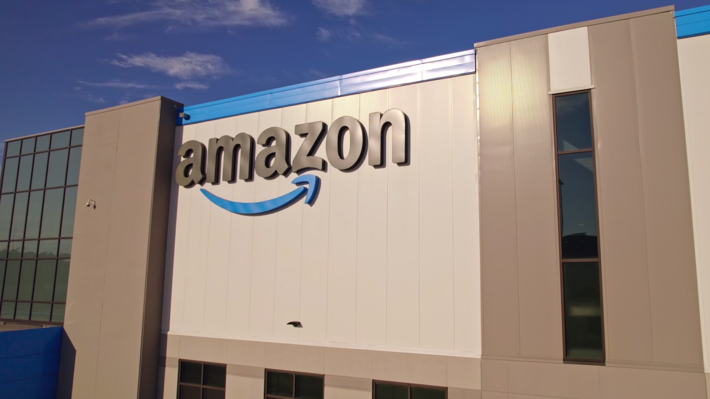 The exterior of an Amazon fulfillment center with the company logo prominently displayed.