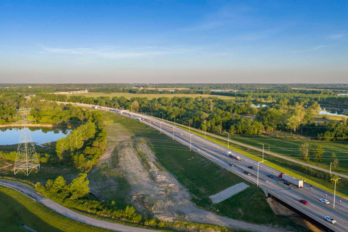 A busy highway running alongside a river and lined with trees and power lines.