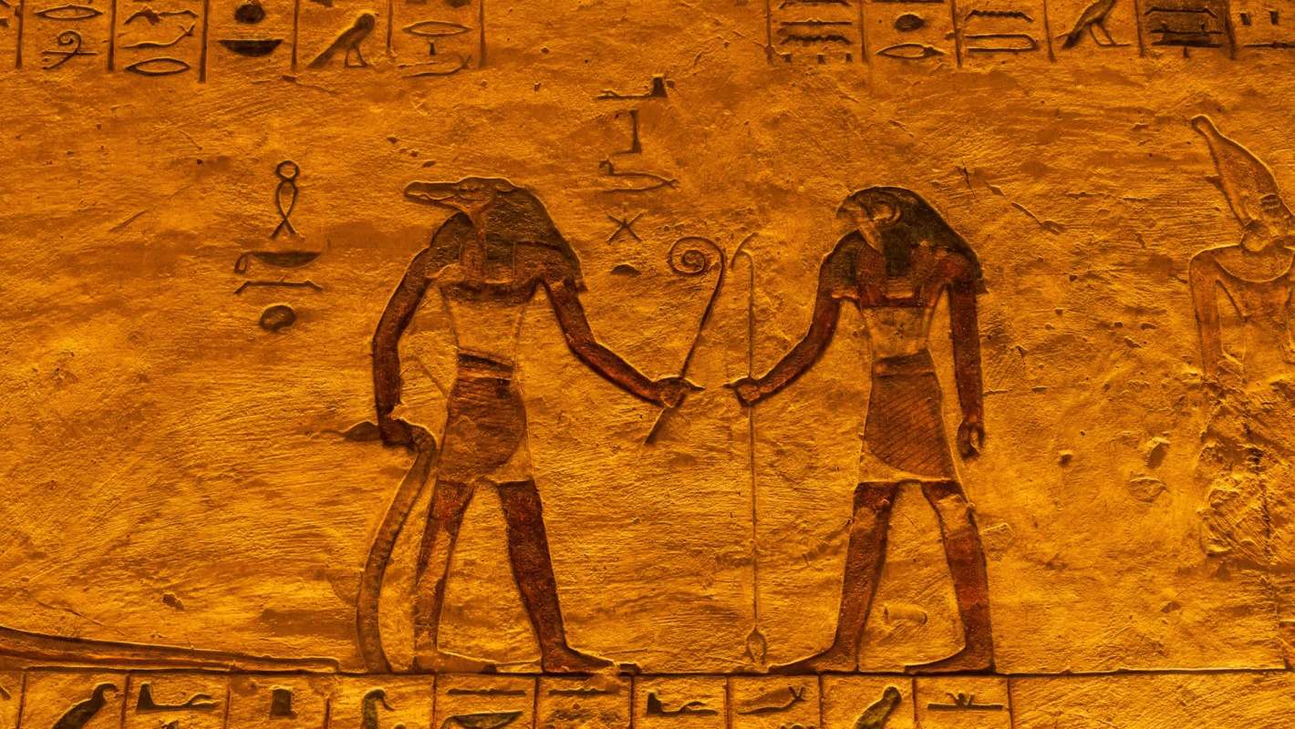 Ancient Egyptian hieroglyphics with figures holding staffs and symbols on a textured gold background.