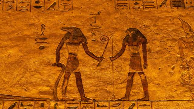 Ancient Egyptian hieroglyphics with figures holding staffs and symbols on a textured gold background.