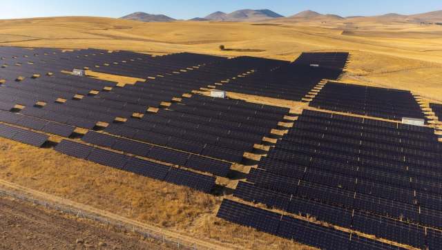 A solar farm with rows of solar panels in a dry, grassy landscape with mountains in the background.