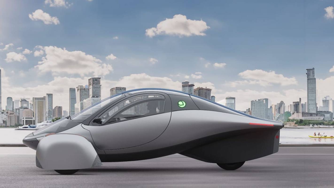 A futuristic gray vehicle is displayed against a city skyline and clear blue sky.