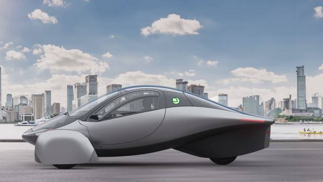 A futuristic gray vehicle is displayed against a city skyline and clear blue sky.