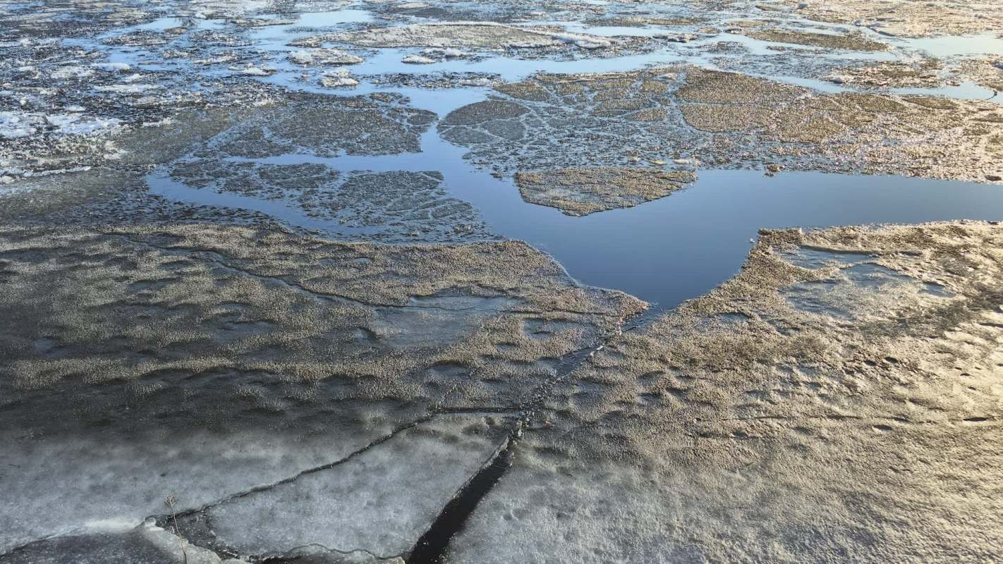 A frozen landscape with patches of ice and water reflecting the surroundings.