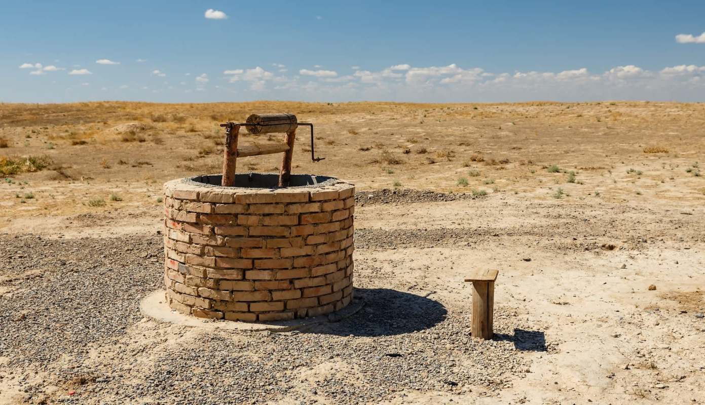 A brick well in a dry landscape with sparse vegetation and a wooden platform nearby.