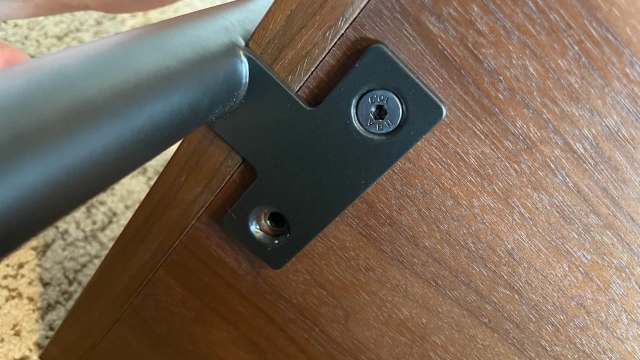 A black metal bracket attached to a wooden surface with a screw.