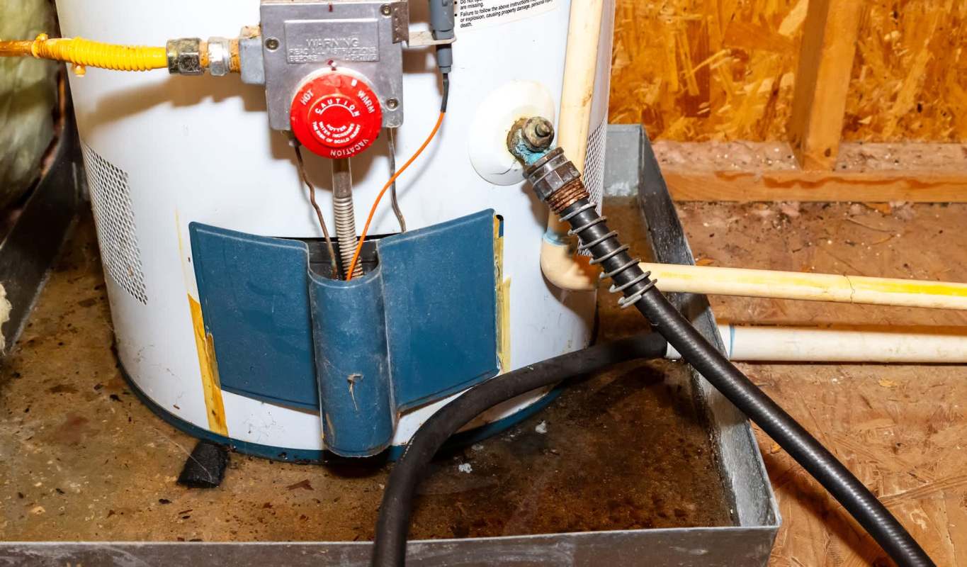 A water heater with connected pipes and a drain pan on a concrete floor.