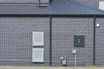 A textured brick wall with utility boxes and a gas meter attached.