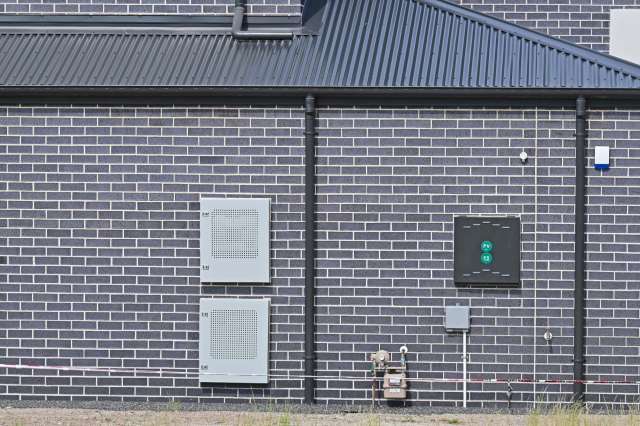 A textured brick wall with utility boxes and a gas meter attached.