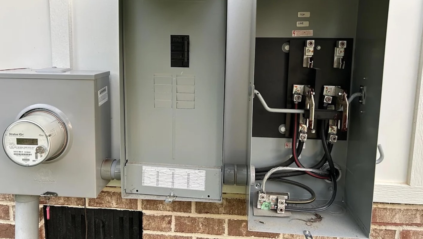 An electrical meter and a circuit breaker panel mounted on a brick wall.