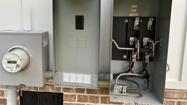An electrical meter and a circuit breaker panel mounted on a brick wall.