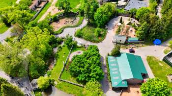 An aerial view of a park featuring pathways, trees, a pond, and several buildings.