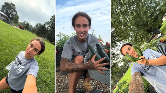 A person holds cucumbers in a garden.