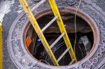 A yellow ladder leads into a round manhole with visible cables inside.