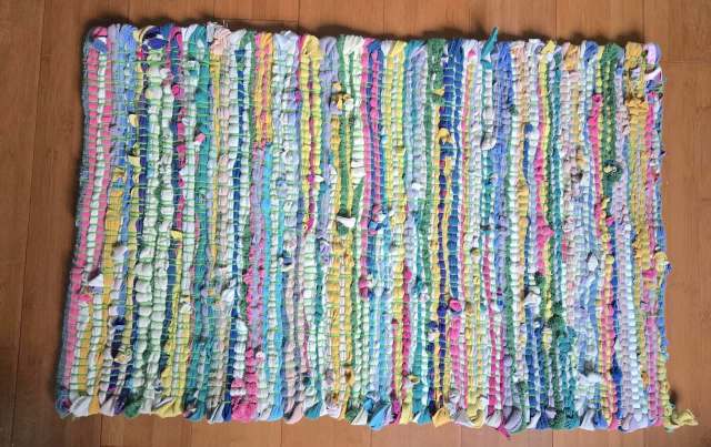 A colorful woven rug made from various fabric scraps laid on a wooden floor.