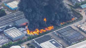 A large fire ignites near industrial buildings, creating thick black smoke and visible flames.