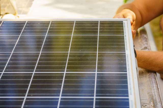 A person handles a solar panel with a grid pattern of photovoltaic cells.